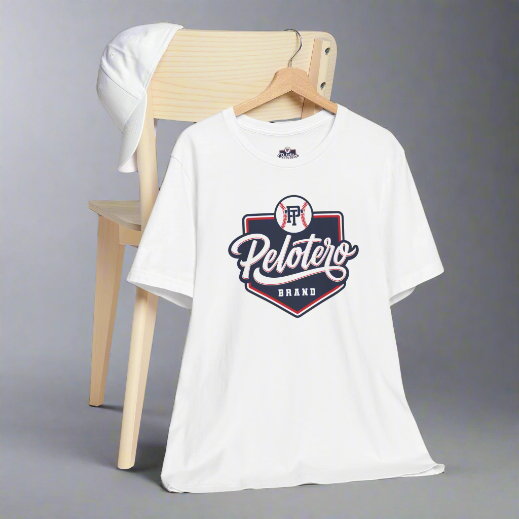 White t-shirt with 'Pelotero Brand' logo on a wooden chair against a gray background